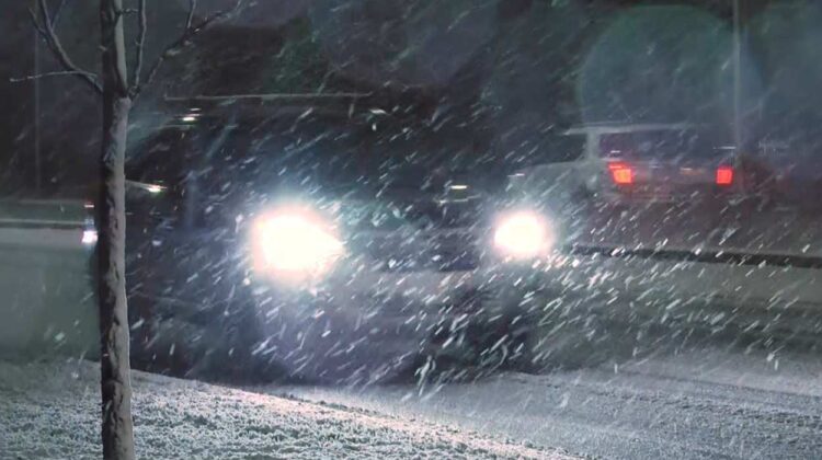 Cars driving on slick roadways at night with snow falling