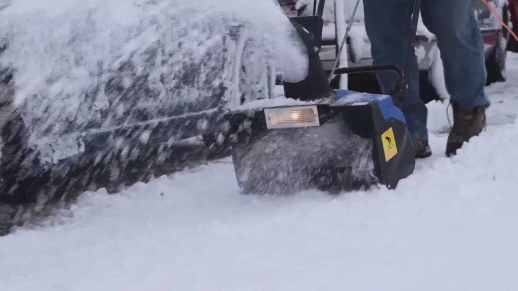 Snowblower removing snow from driveway, blowing snow in air