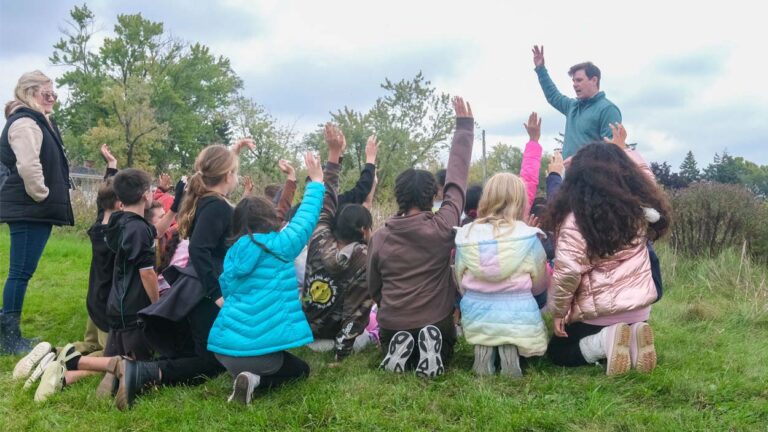 Children campers at The Conservation Foundation raise their hands while looking at counselor