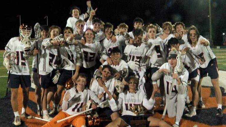 Huskies lacrosse players celebrate with the Naperville Cup trophy.