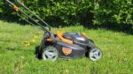 Lithium-ion battery powered lawn mower sits in the middle of a yard.