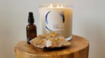 Close up of a NOW Massage lit candle, aromatherapy bottle, and crystals.