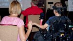 A woman holds the hand of a child in a wheelchair with their back to the camera.
