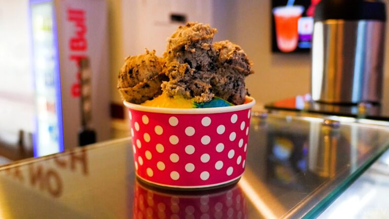 A red paper ice cream cup with white polka dots featuring superman ice cream topped with oreo cookie dough.