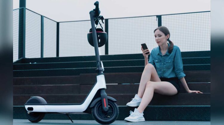 Woman sitting on steps looking at phone with e-scooter in front of her