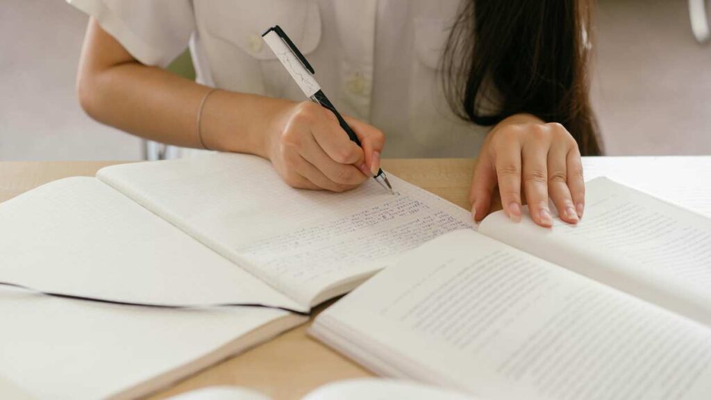 Close up notebook and books with student writing in notebook