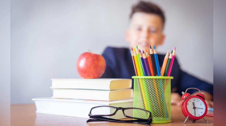 student sitting at desk with books, apple, glasses and pencil holder