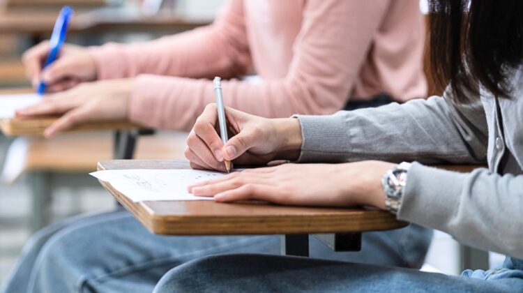 Close up of students writing on papers on desks.