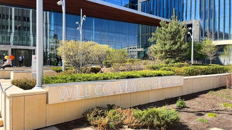 A picture of the Will County Courthouse sign with the building in the back for a story about Neuqua Valley High School teacher William Schaub.