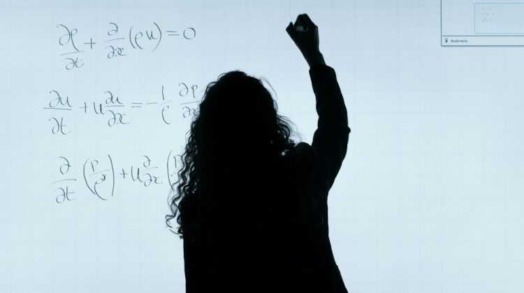 Outline - dark profile from behind of a teacher/educator writing equations on a whiteboard