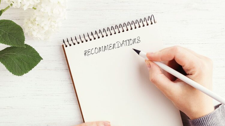 Hand writing word recommendations on notebook with flower in top left of image