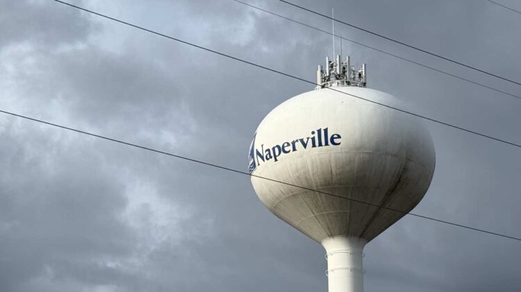 Cell phone tower components atop Naperville water tower with power lines in foreground