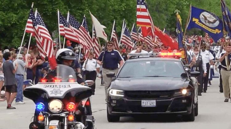 Motorcyclist, car, and a lineup of flags with marchers at the Memorial Day Parade in Naperville
