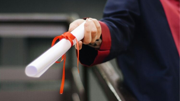 Rolled up piece of paper tied with bow held in hand - like a diploma - for story on National Merit Scholarship winners