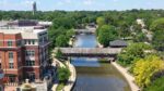 Wide drone shot of Naperville overlooking Riverwalk, covered bridge with Moser Tower in the distance